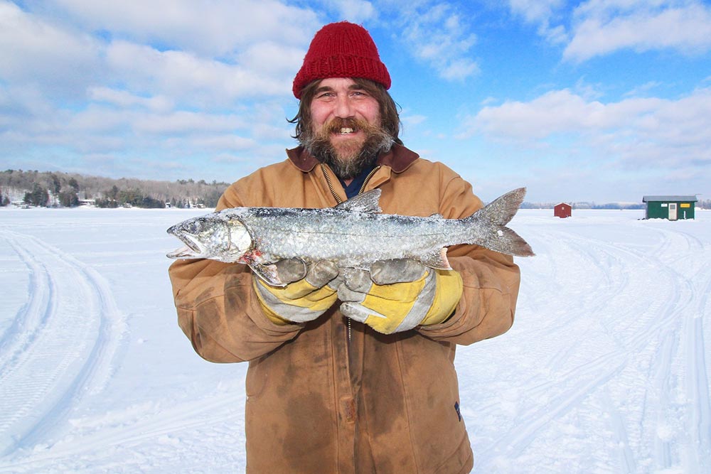 Fishing-man-ice-fishing-canada-holding-trout-winter-smiling.