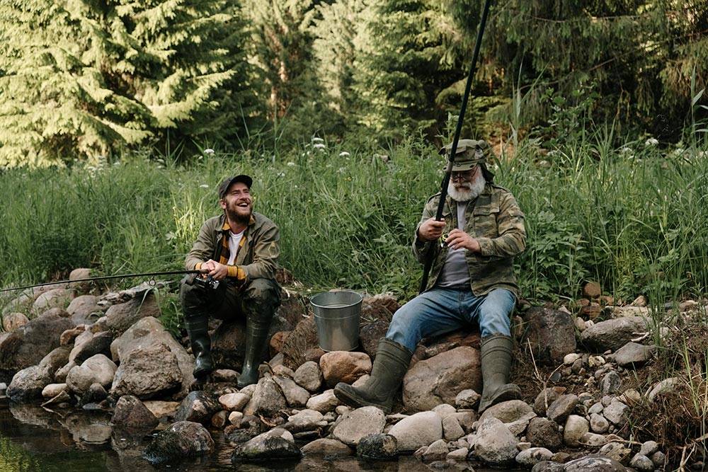 Fishing-two-men-in-brown-jacket-and-blue-denim-jeans-sitting-on-brown-rock.