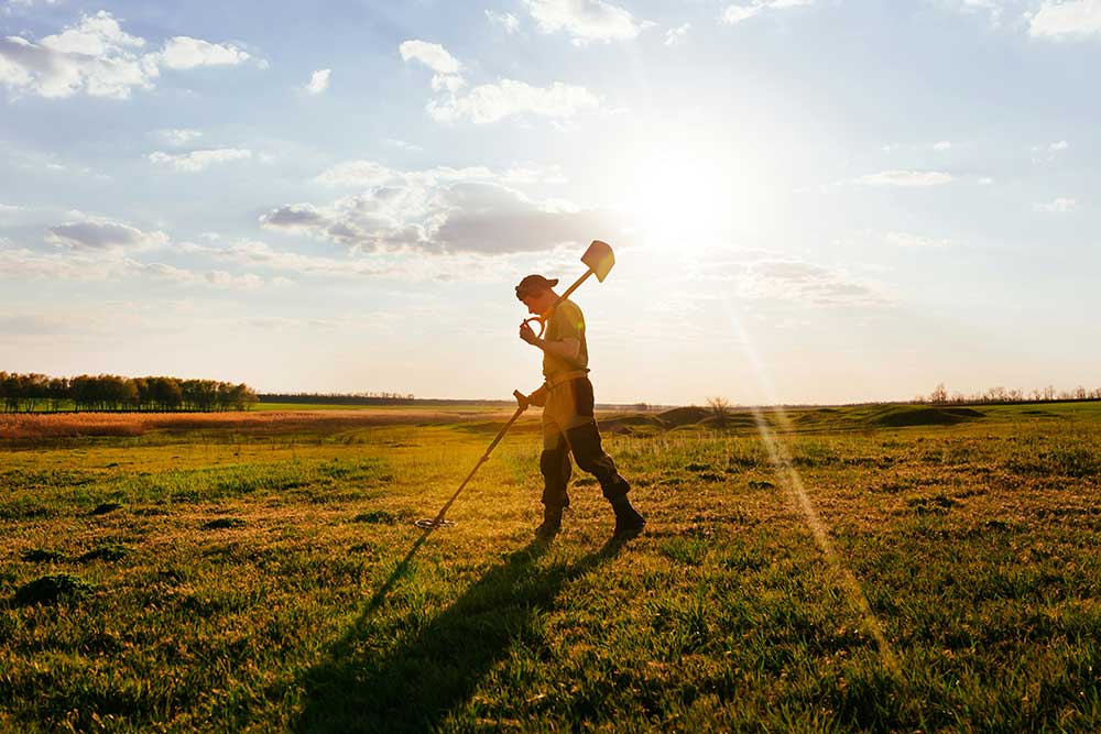 Man walking through field using a metal detector.
