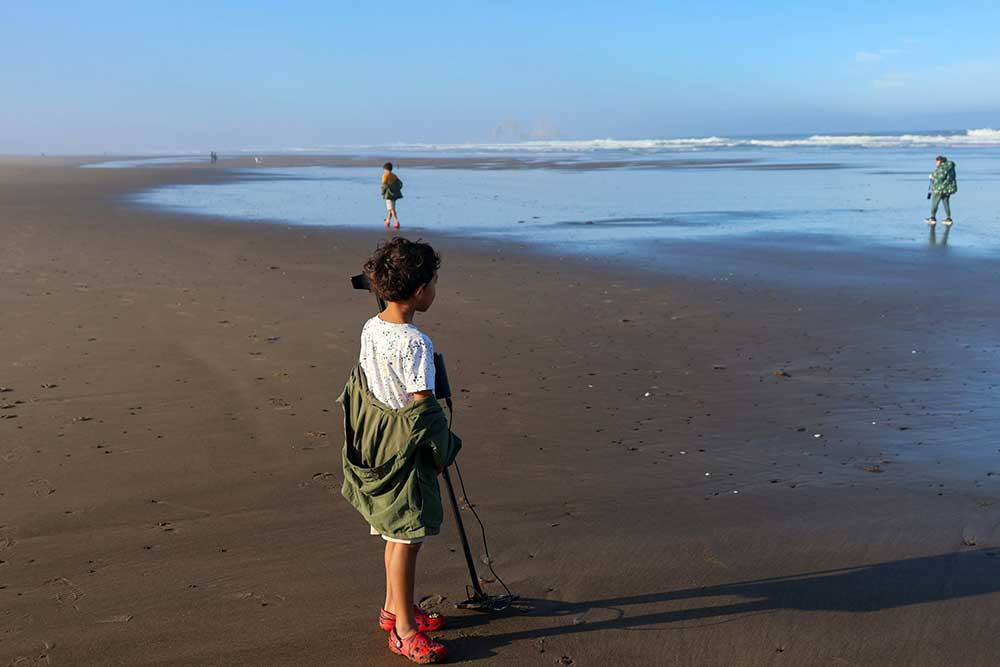 Young boy on the beach metal detecting in the sand.