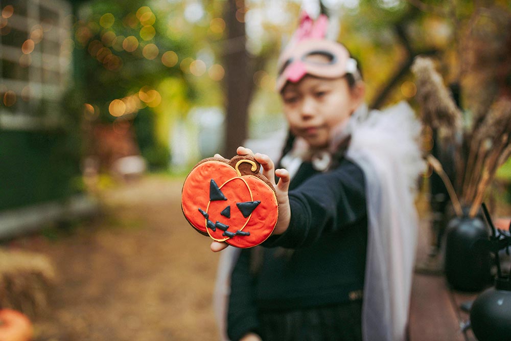 young-girl-in-halloween-costume-holding-jack-o-lantern-cookie